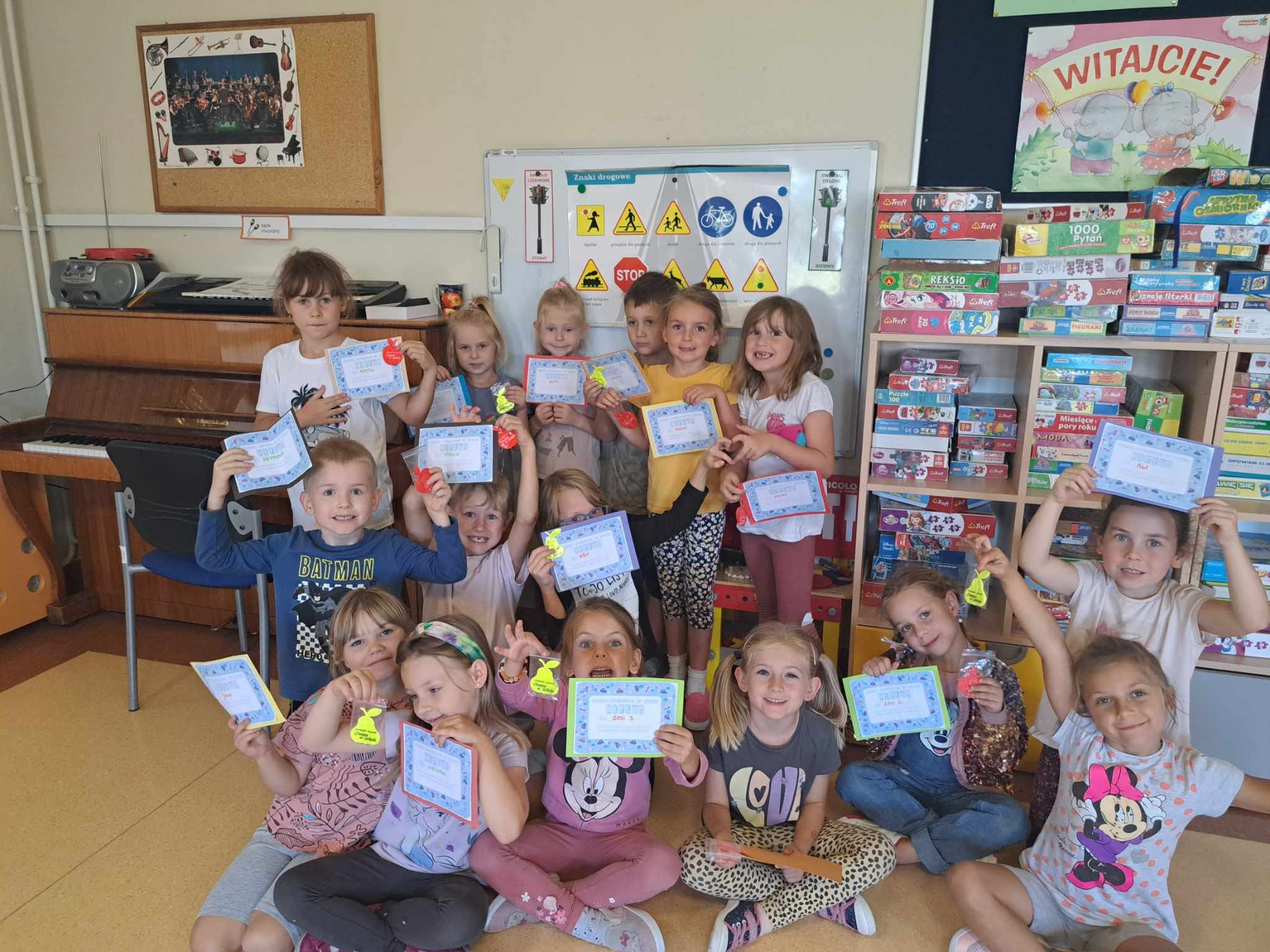 Dzieci w sali lekcyjnej trzymają w rękach dyplomy.