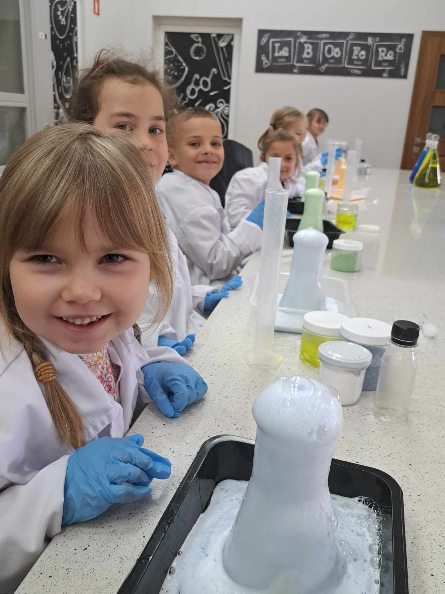 Dzieci w białych fartuchach wykonują eksperymenty chemiczne