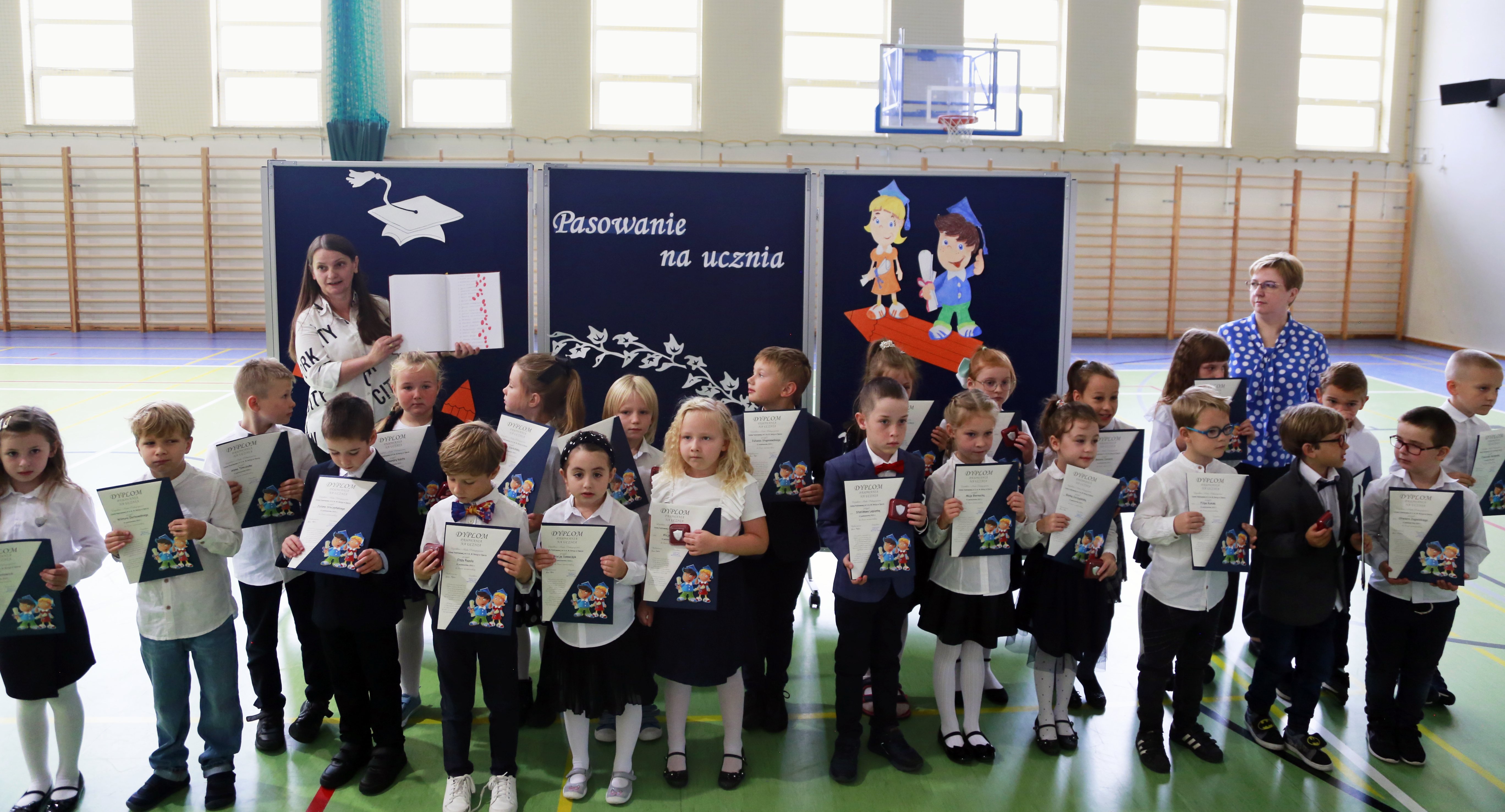 Uczniowie klasy pierwszej z nauczycielami na tle dekoracji